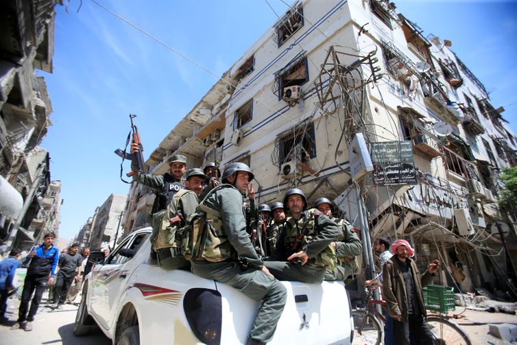 Members of the Syrian police hold their weapons as they sit on a back of a truck at the city of Douma, Damascus, Syria April 16, 2018. REUTERS/Ali Hashisho