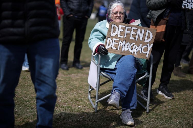 79-year-old Christine Hughes holds a sign as she attends a demonstration during the day of 